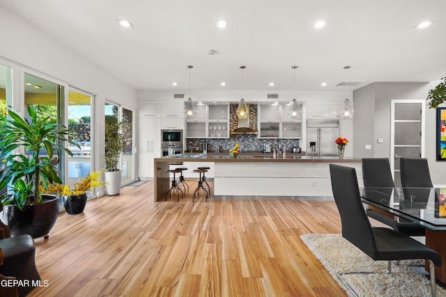 kitchen featuring stainless steel appliances, white cabinets, wall chimney range hood, decorative backsplash, and a large island with sink