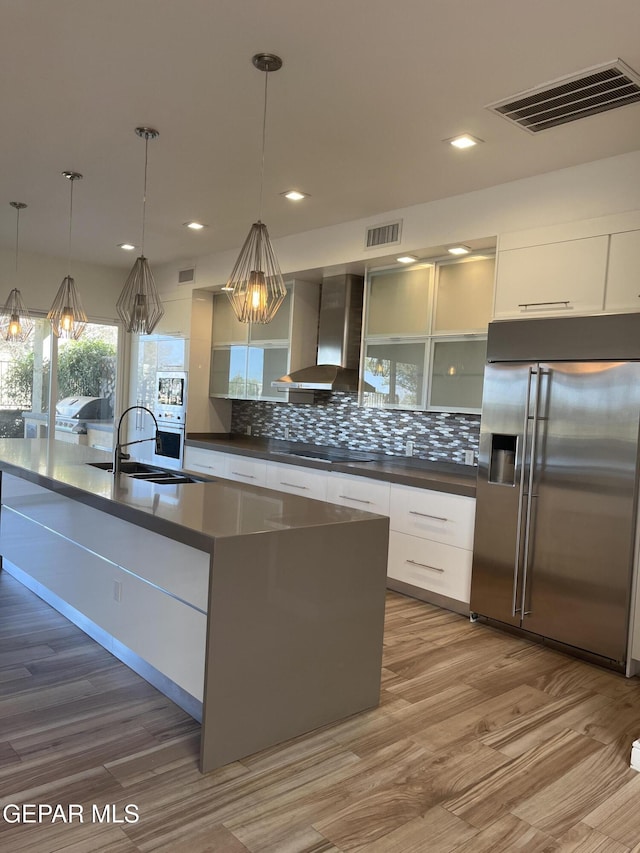 kitchen with wall chimney exhaust hood, modern cabinets, visible vents, and high end fridge