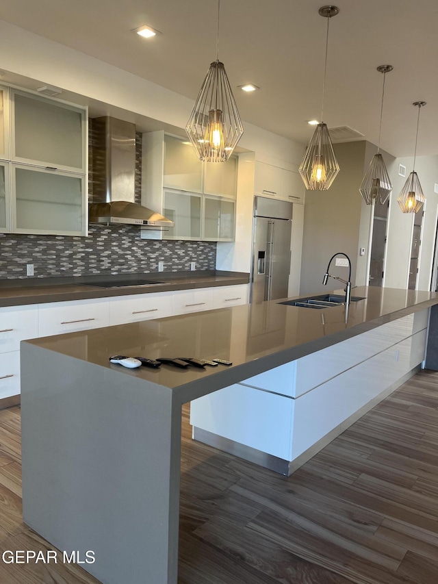 kitchen featuring wall chimney range hood, a large island, stainless steel built in fridge, dark countertops, and modern cabinets