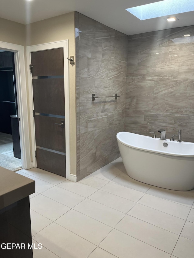 full bathroom featuring a skylight, a freestanding bath, tile walls, and tile patterned floors