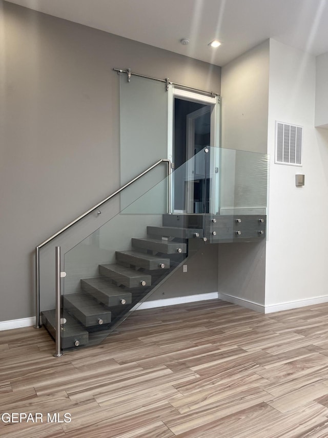 staircase featuring wood finished floors, visible vents, baseboards, and a barn door