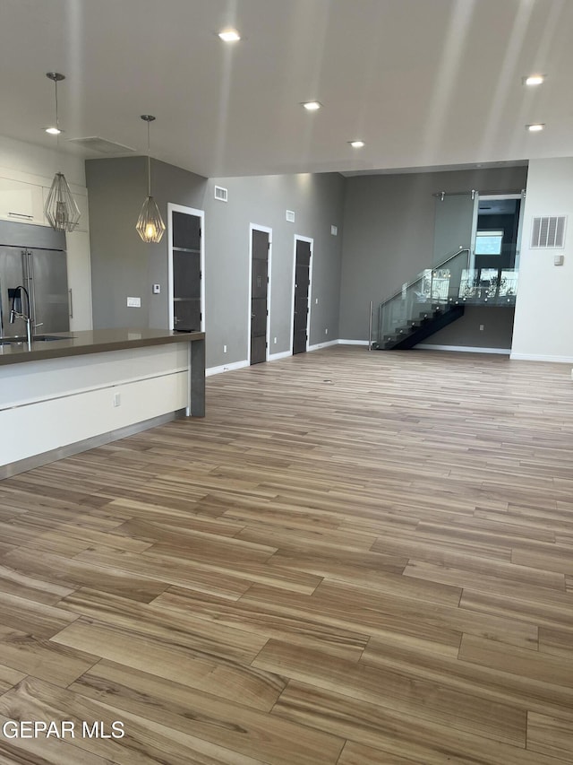 unfurnished living room with light wood-type flooring, visible vents, and baseboards