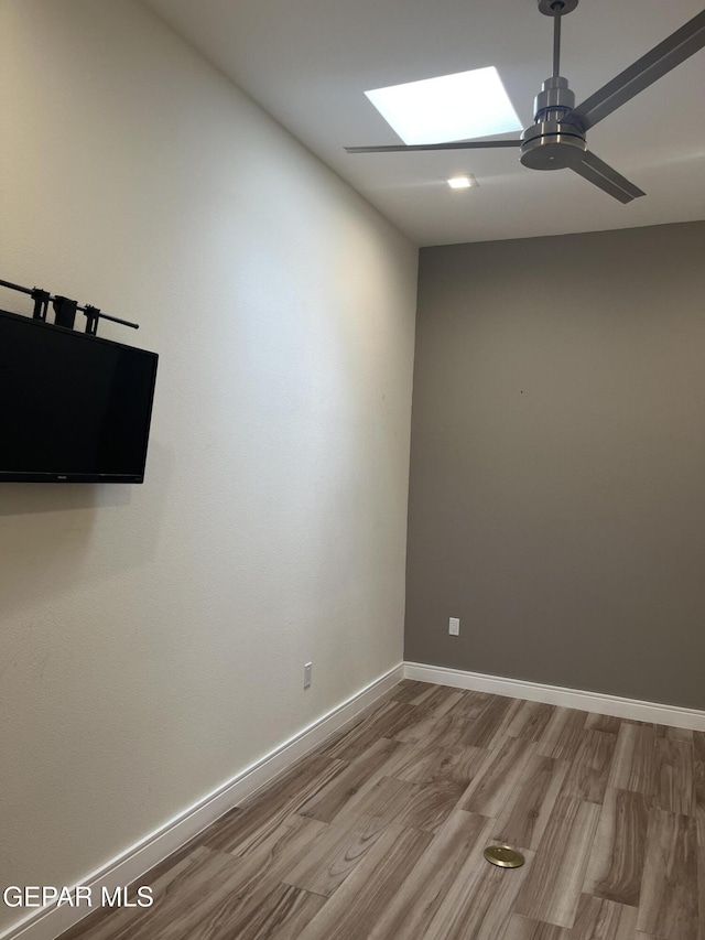 spare room with a ceiling fan, a skylight, baseboards, and wood finished floors