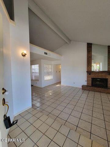 unfurnished living room featuring light tile patterned floors, lofted ceiling with beams, a fireplace, and visible vents