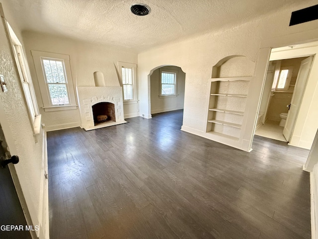 unfurnished living room featuring a textured ceiling, a textured wall, dark wood-type flooring, a fireplace with flush hearth, and built in features