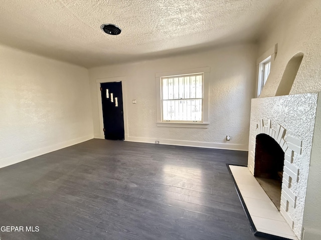 unfurnished living room featuring baseboards, a textured wall, dark wood-style floors, a textured ceiling, and a fireplace