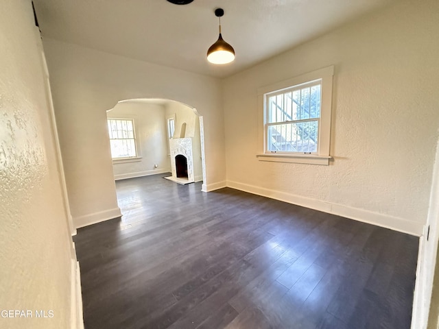 unfurnished living room featuring arched walkways, a textured wall, dark wood-type flooring, a fireplace with flush hearth, and baseboards