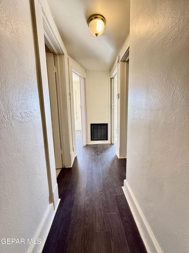 corridor with baseboards, visible vents, dark wood finished floors, and a textured wall