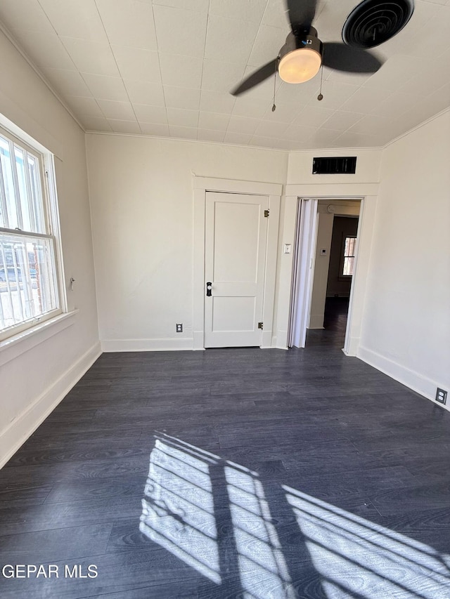 unfurnished room featuring dark wood-style flooring, visible vents, and baseboards