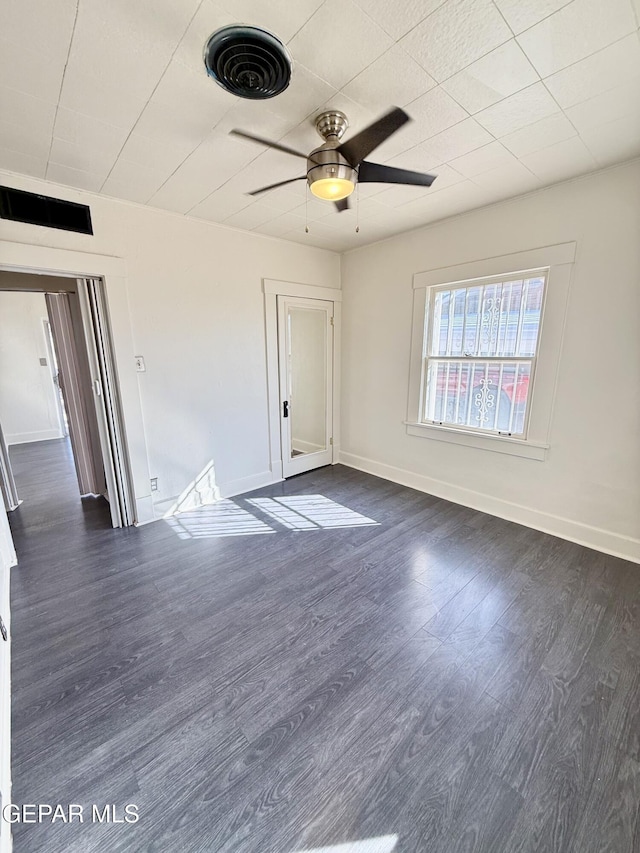 empty room featuring a ceiling fan, dark wood-style flooring, visible vents, and baseboards