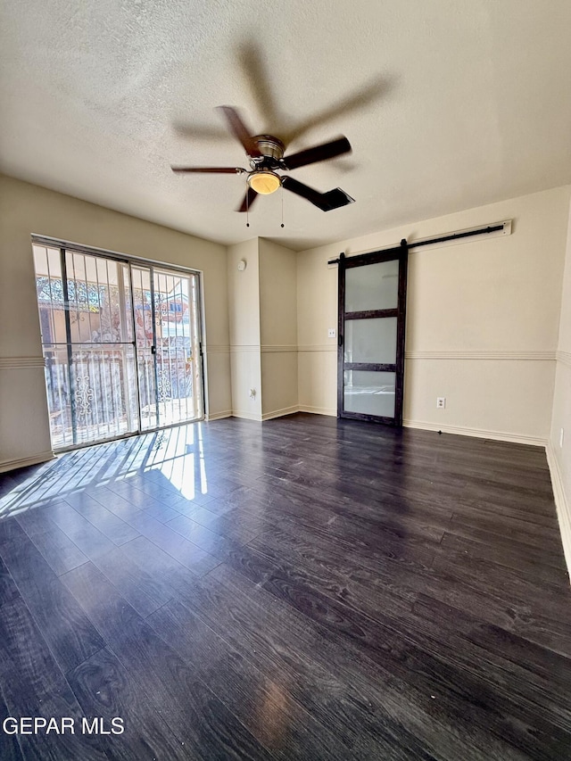 unfurnished room with dark wood finished floors, a barn door, a ceiling fan, a textured ceiling, and baseboards