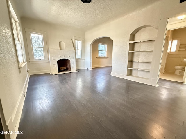 unfurnished living room with a healthy amount of sunlight, built in features, dark wood finished floors, and a textured ceiling