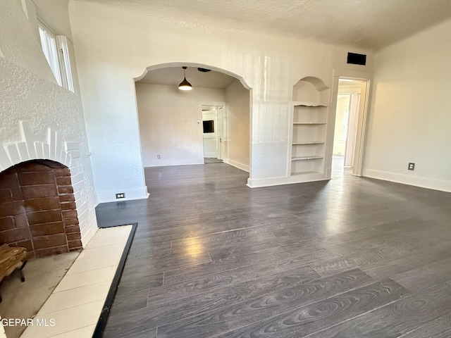 unfurnished living room featuring baseboards, built in shelves, arched walkways, and dark wood-style flooring