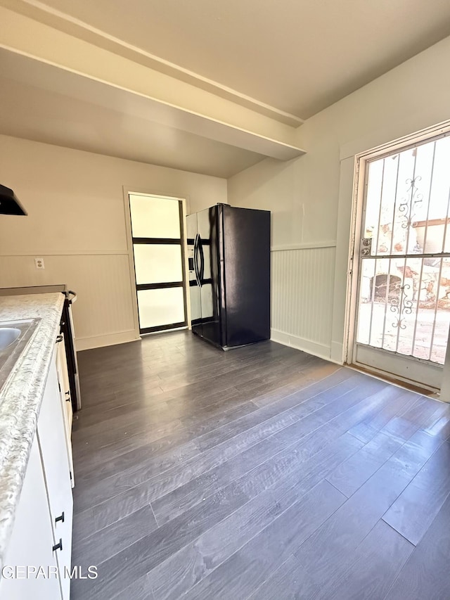 kitchen with white cabinets, dark wood-style flooring, black fridge, and wainscoting