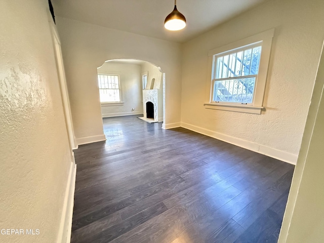 unfurnished living room featuring baseboards, arched walkways, a textured wall, dark wood-style flooring, and a fireplace