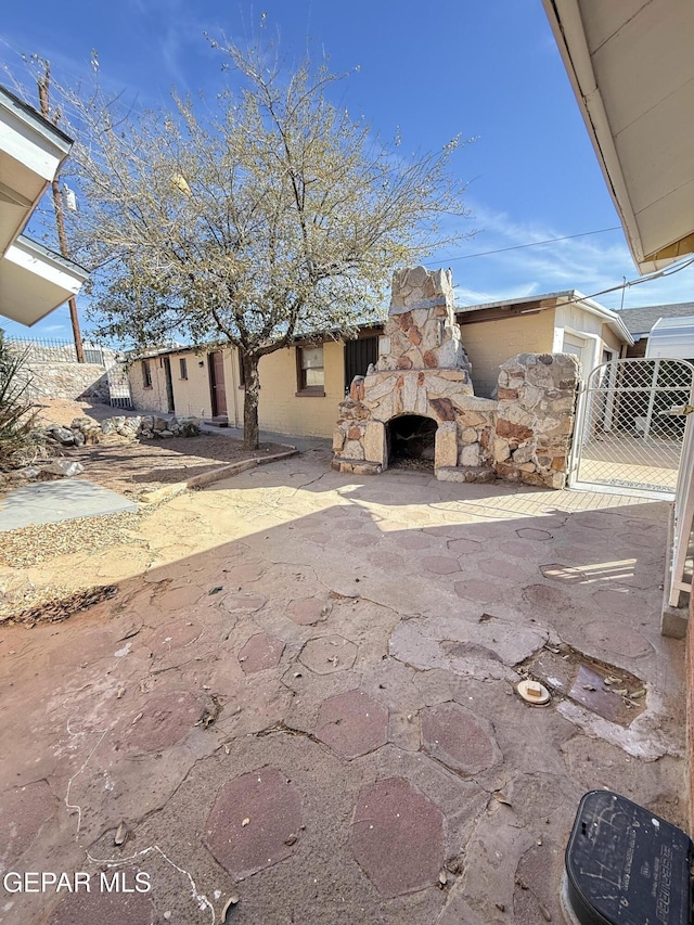 view of patio featuring an outdoor stone fireplace, fence, and a gate