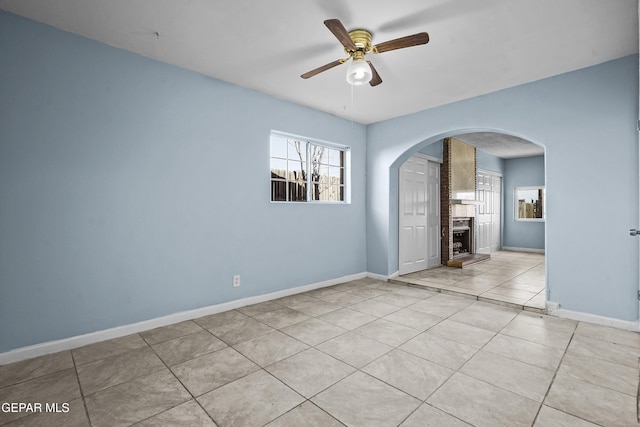 unfurnished room featuring baseboards, arched walkways, a large fireplace, and ceiling fan