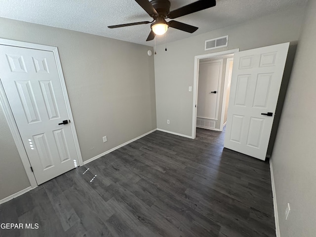 unfurnished bedroom with a textured ceiling, dark wood-type flooring, visible vents, and baseboards