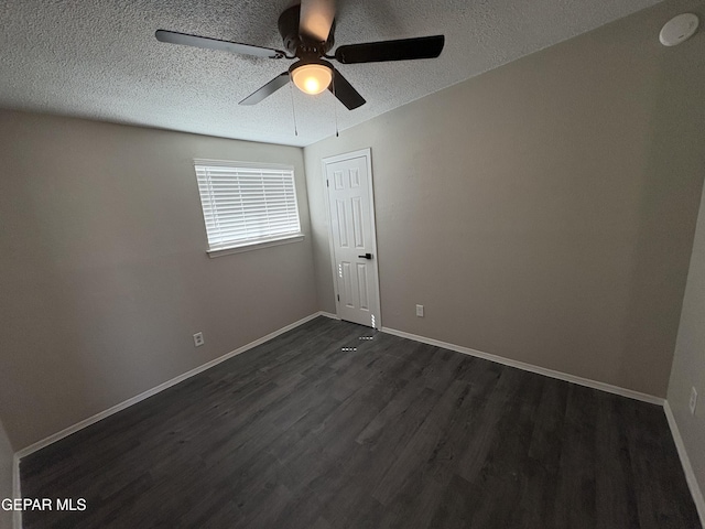 empty room featuring a ceiling fan, a textured ceiling, baseboards, and dark wood-type flooring