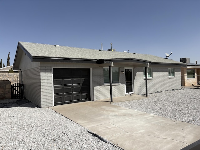 single story home featuring a garage, concrete driveway, brick siding, and central AC