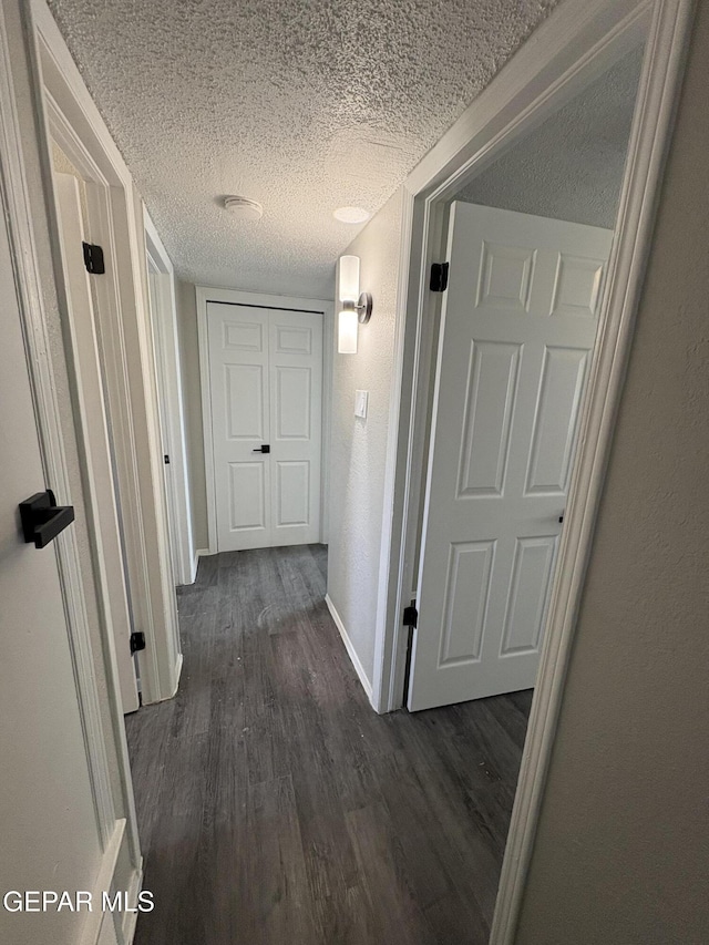 corridor with dark wood-style floors, a textured wall, a textured ceiling, and baseboards