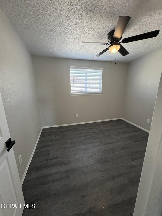 empty room with a textured ceiling, dark wood-type flooring, a ceiling fan, and baseboards