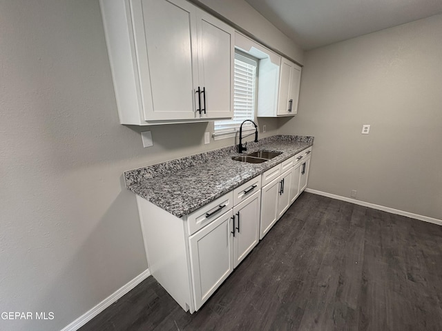 kitchen featuring baseboards, white cabinets, light stone counters, dark wood-type flooring, and a sink