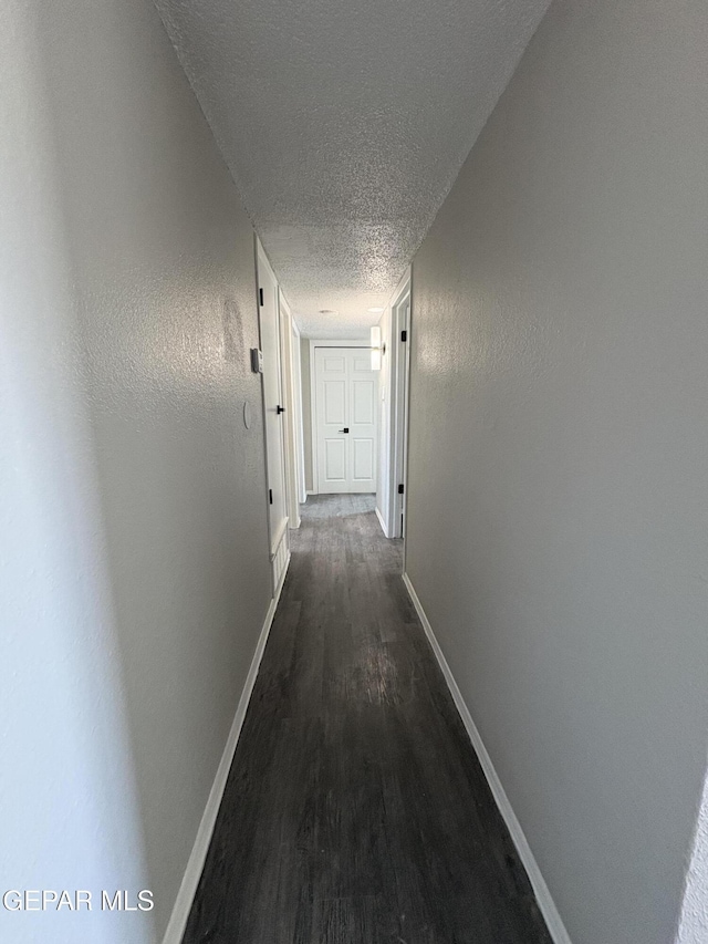 corridor with a textured ceiling, a textured wall, dark wood finished floors, and baseboards