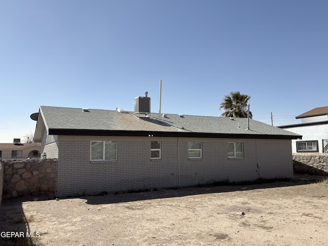 back of property featuring cooling unit, brick siding, fence, and roof with shingles