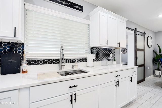 kitchen featuring decorative backsplash, a barn door, white cabinets, a sink, and light stone countertops