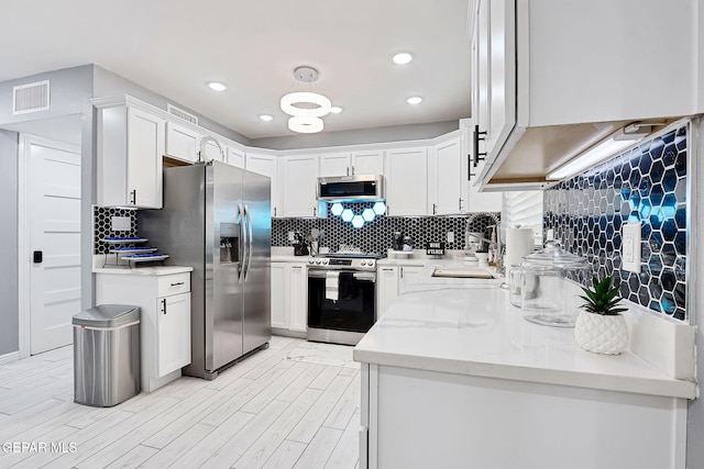 kitchen with stainless steel appliances, a sink, visible vents, white cabinets, and decorative backsplash