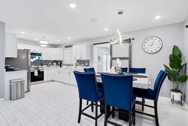 dining space with light wood finished floors, a barn door, baseboards, and recessed lighting