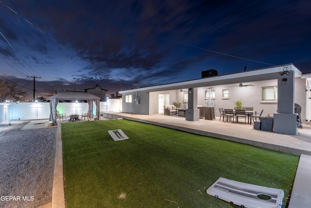 rear view of property with outdoor lounge area, fence, a gazebo, a lawn, and stucco siding