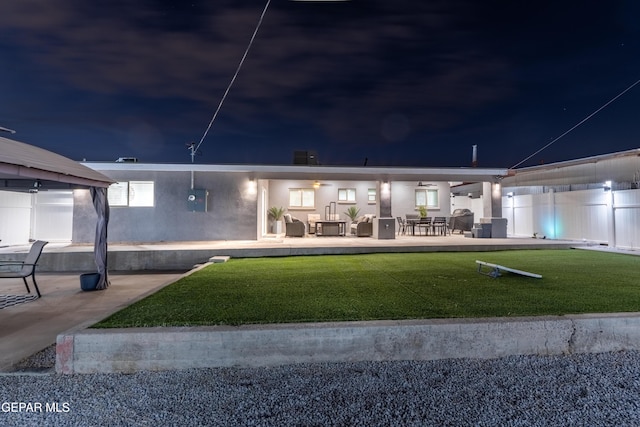 back of house at twilight featuring a patio area, fence, a lawn, and stucco siding