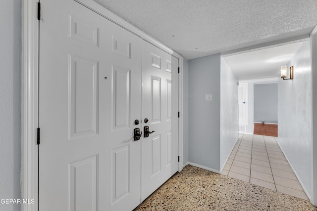 hall with a textured ceiling, baseboards, and light tile patterned floors