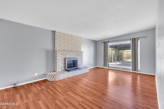 unfurnished living room with a brick fireplace, a textured ceiling, baseboards, and wood finished floors