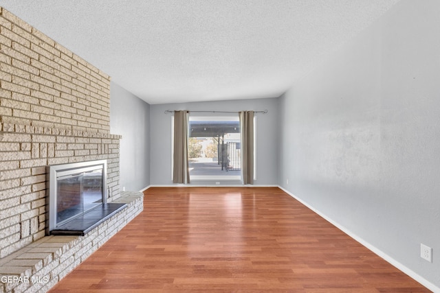 unfurnished living room featuring a brick fireplace, a textured ceiling, baseboards, and wood finished floors