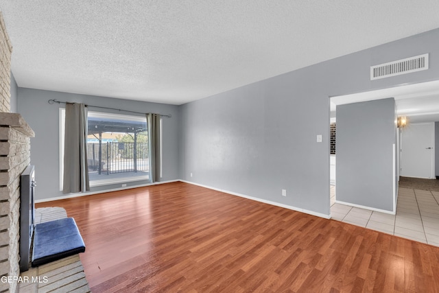 unfurnished living room featuring a textured ceiling, a fireplace, wood finished floors, and visible vents