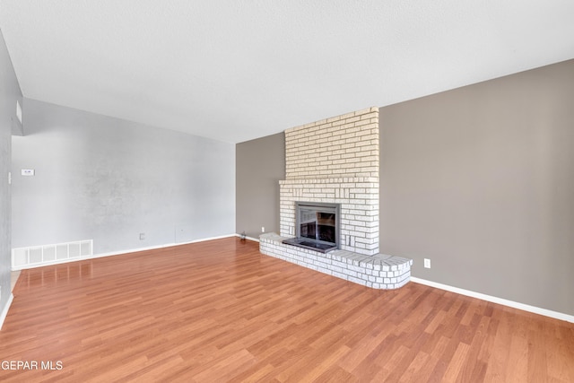 unfurnished living room featuring a brick fireplace, baseboards, visible vents, and light wood-style floors