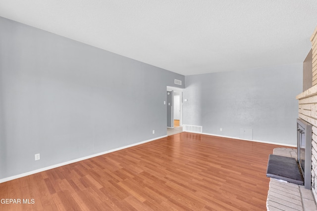 unfurnished living room featuring baseboards, a fireplace, visible vents, and light wood-style floors