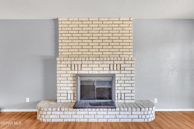 interior details featuring a brick fireplace, a textured ceiling, baseboards, and wood finished floors