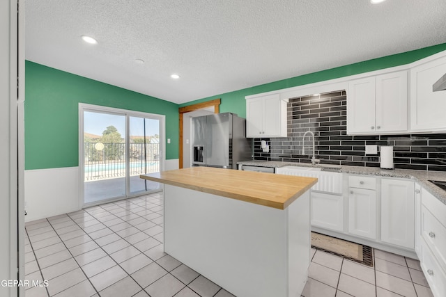 kitchen featuring butcher block countertops, stainless steel fridge, a sink, and white cabinetry