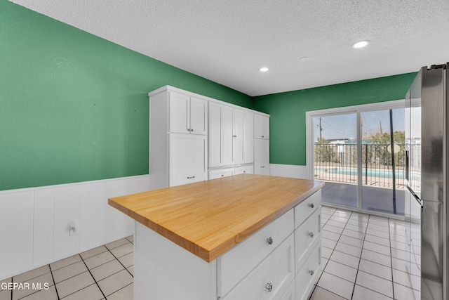 kitchen with a textured ceiling, butcher block countertops, white cabinets, wainscoting, and freestanding refrigerator