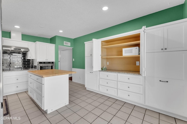 kitchen with open shelves, light tile patterned floors, visible vents, white cabinets, and stainless steel oven