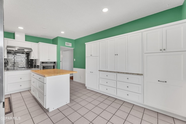 kitchen featuring visible vents, white cabinets, light tile patterned flooring, butcher block countertops, and oven