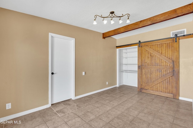 tiled empty room featuring beam ceiling, visible vents, a barn door, a textured ceiling, and baseboards