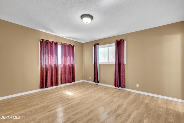 unfurnished room with a textured ceiling, light wood-style flooring, and baseboards