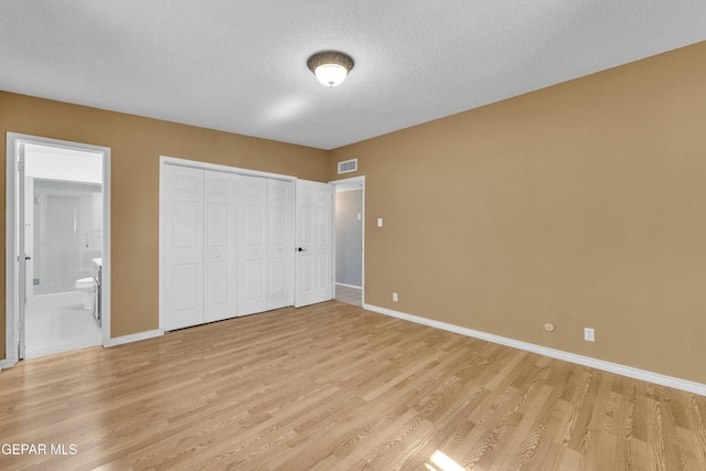 unfurnished bedroom with a textured ceiling, ensuite bathroom, visible vents, baseboards, and light wood-style floors