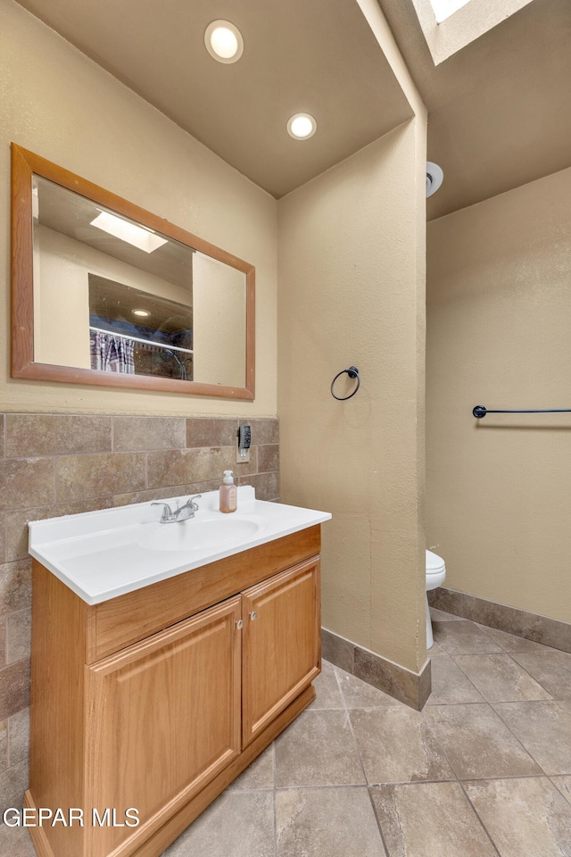 bathroom featuring a skylight, tile walls, vanity, and toilet