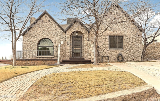 english style home with stone siding and a front yard